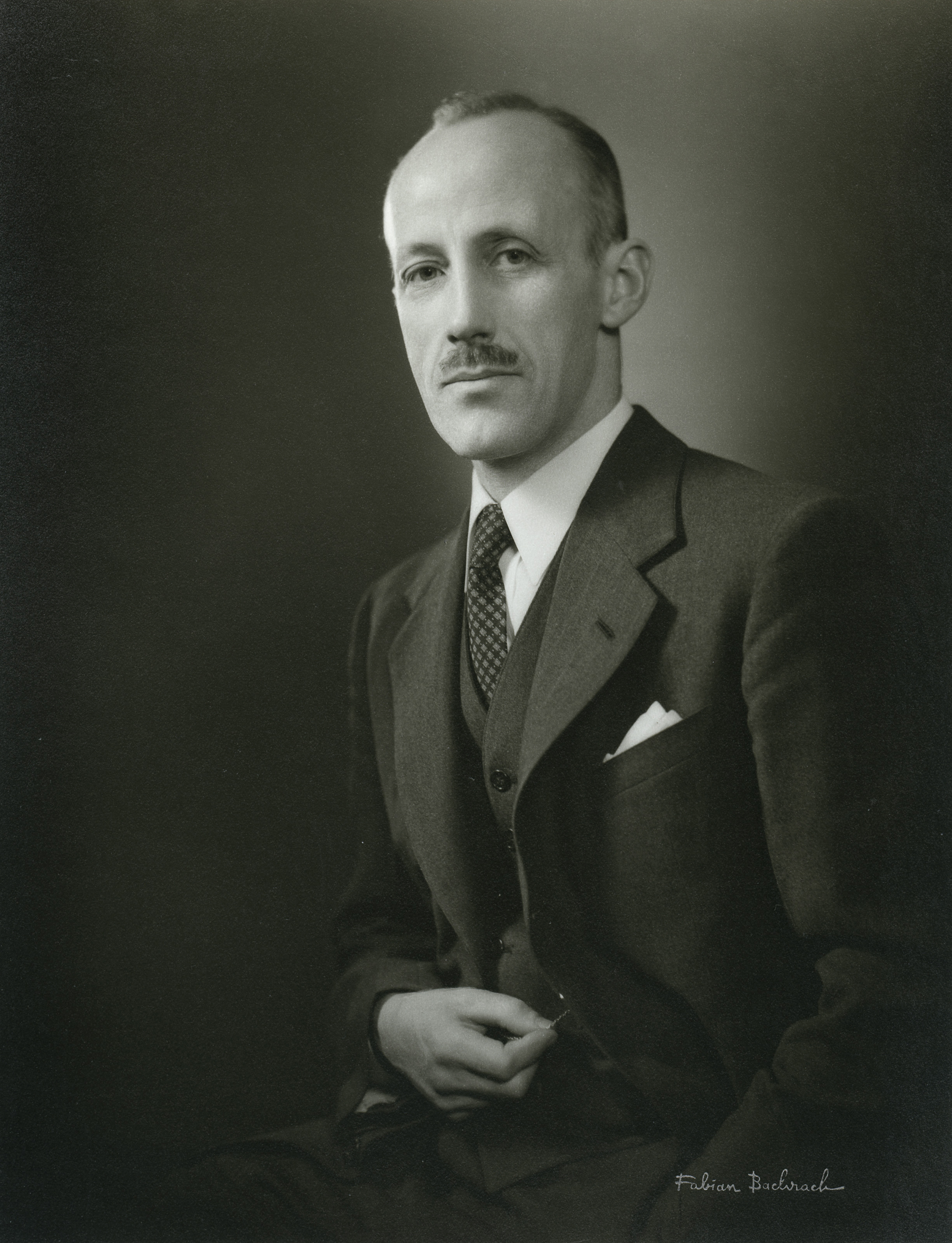 black and white portrait of a seated white man with a moustache, wearing a three-piece suit